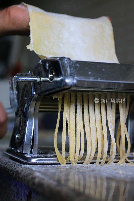 意大利面食机上挂着生面食的面粉带，面目全非的人用擀好的面团做家常宽面条/扁面条，厨房场景